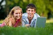 A couple relaxing in the park with a laptop, lying on the grass