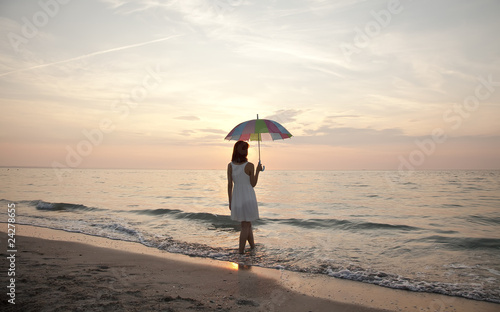 Photo: Young beautiful girl on the beach at sunrise with umbrella. Young beautiful girl on the beach at sunrise with umbrella.