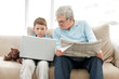 Old man sitting with a newspaper while a little boy using a lapt