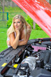 Young beautiful woman standing near red car and looking under ho