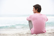 Young Man On Holiday Sitting On Winter Beach