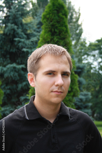 Photo: Portrait of beautiful young man against summer park Portrait of beautiful young man against summer park