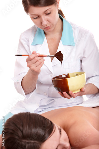 Photo: Girl having chocolate facial mask apply by beautician. Girl having chocolate facial mask apply by beautician.