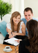 Happy young couple signing a contract sitting in the living room Happy young couple signing a contract sitting in the living room