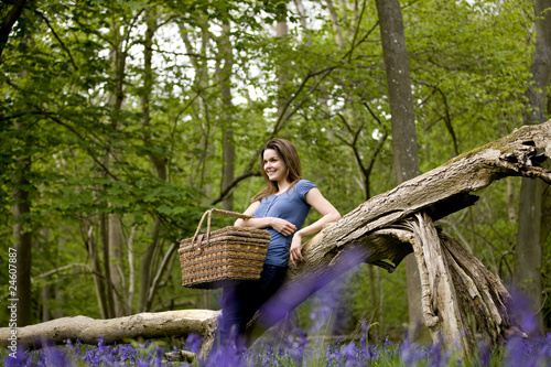 Foto: A young woman leaning against a tree, holding a picnic basket A young woman leaning against a tree, holding a picnic basket