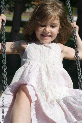 Photo: Cheerful little girl swinging, looking away from the camera Cheerful little girl swinging, looking away from the camera