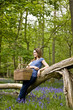 A young woman leaning against a tree, holding a picnic basket