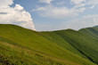 Mountain ridge slopes covered by green grass and cloudy blue sky Mountain ridge slopes covered by green grass and cloudy blue sky
