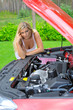 Young beautiful woman standing near red car and looking under ho