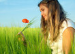 Young woman in green field holding poppy flower