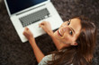 AN attractive young woman lying on floor with a laptop looking u