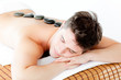 Resting young man lying on a massage table with hot stone on his Resting young man lying on a massage table with hot stone on his