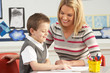 Male Primary School Pupil And Teacher Working At Desk In Classro