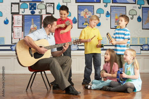 Photo: Male Teacher Playing Guitar With Pupils Having Music Lesson In C Male Teacher Playing Guitar With Pupils Having Music Lesson In C