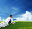 Young man use a notebook on green field