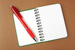 Opened notebook squared pagewith red pen over it on brown backgr