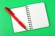 Opened notebook squared pagewith red pen over it on green backgr