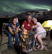 Family at campfire in mountains with northern lights