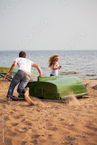 Photo: young couple fun and run around old boat on a beach young couple fun and run around old boat on a beach