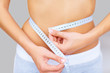 Caucasian woman measuring her waistline with a tape
