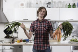 Photo: germany, berlin, young man in kitchen holding bunch of carrots and spring onions, laughing, portrait germany, berlin, young man in kitchen holding bunch of carrots and spring onions, laughing, portrait