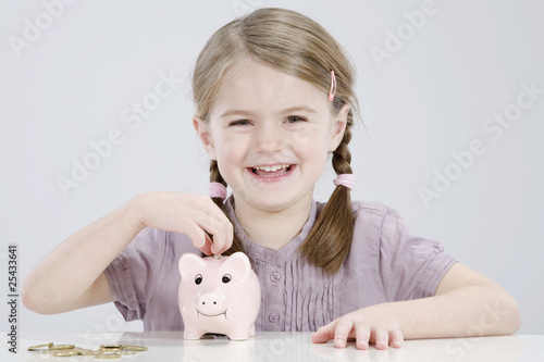 Photo: girl (4-5) putting coin into piggy bank, smiling, portrait girl (4-5) putting coin into piggy bank, smiling, portrait