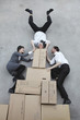 Photo: three business people on cardboard boxes, man doing handstand, smiling, portrait, elevated view three business people on cardboard boxes, man doing handstand, smiling, portrait, elevated view