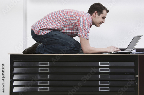 Photo: man kneeling on desk using laptop man kneeling on desk using laptop