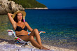 Woman in black bikini and straw hat tans on deckchair in beauty