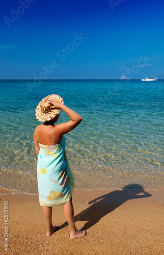 Photo: Young woman in pareo and hat looking into the blue sea Young woman in pareo and hat looking into the blue sea