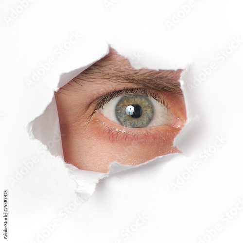 Foto: Eye looking through a hole in paper Eye looking through a hole in paper