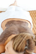 Young caucasian woman lying on a massage table with mud on her b