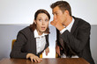 Businessman whispering in businesswoman's ear at office