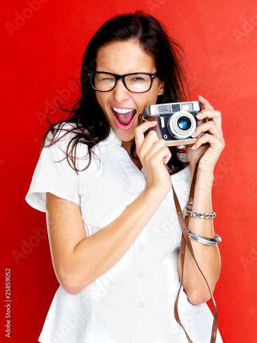Photo: Happy young woman winking with a camera in hand Happy young woman winking with a camera in hand