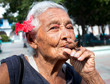 Old wrinkled woman with red flower smoking cigar Old wrinkled woman with red flower smoking cigar