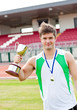 Delighted male athlete holding a cup and a medal standing