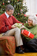 Senior couple exchanging gifts by Christmas tree