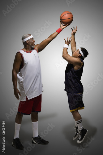 Photo: Tall basketball player keeping ball from shorter player Tall basketball player keeping ball from shorter player