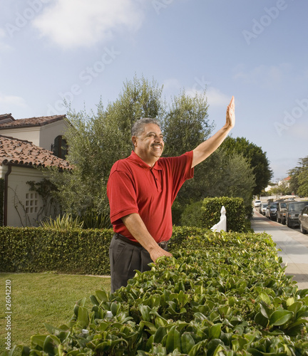 Photo: Middle-aged Hispanic man waving next to hedge Middle-aged Hispanic man waving next to hedge
