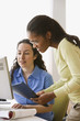 Two businesswomen with paperwork looking at computer