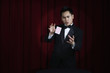 Asian magician in tuxedo doing magic trick onstage