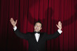 Hispanic man in tuxedo singing with arms outstretched onstage