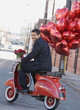 Mixed race man riding scooter with heart-shaped balloons