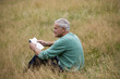A senior man sitting on the grass, reading a book