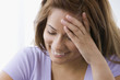 Smiling Hispanic woman looking down with head in hands