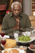 African man saying grace at dinner table