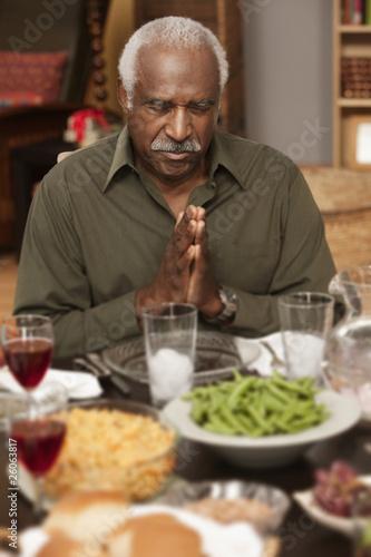 Photo: African man saying grace at dinner table African man saying grace at dinner table