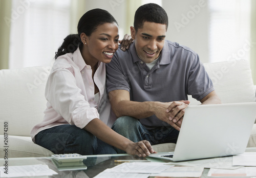 Photo: Couple paying bills online in living room Couple paying bills online in living room