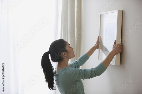 Photo: Mixed race woman hanging picture on wall Mixed race woman hanging picture on wall