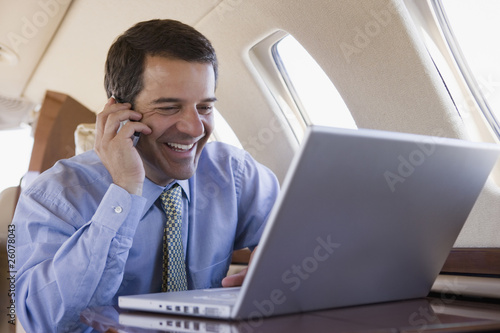 Photo: Hispanic businessman using laptop and cell phone on airplane Hispanic businessman using laptop and cell phone on airplane